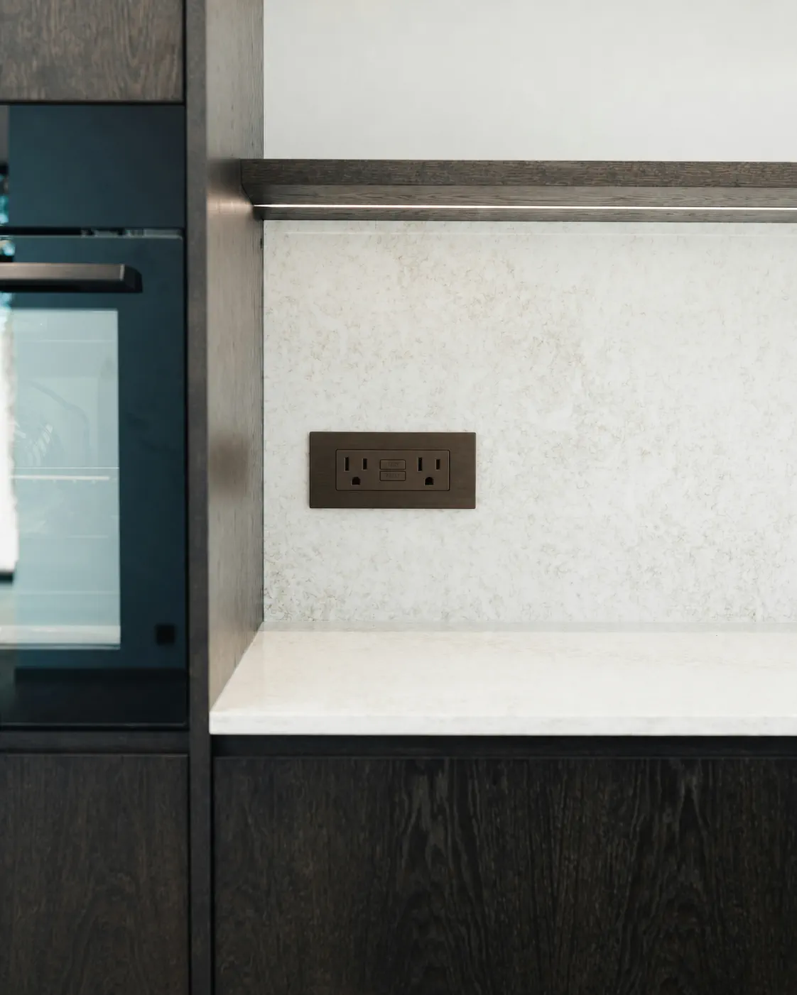 Dark oak kitchen detail with integrated light and a pale stone surface